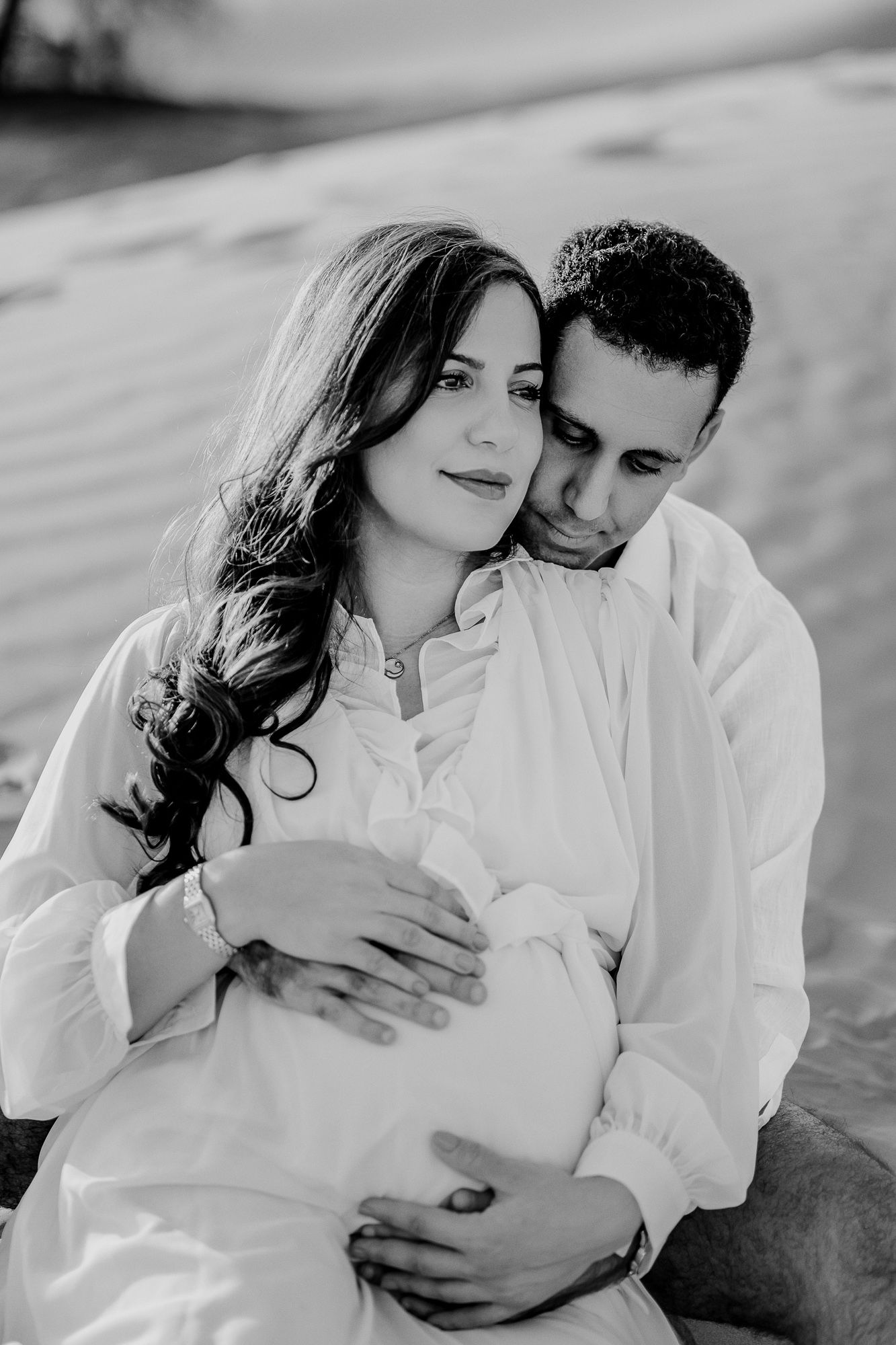 A romantic black and white photo series showing a couple in white clothing embracing tenderly on a beach.