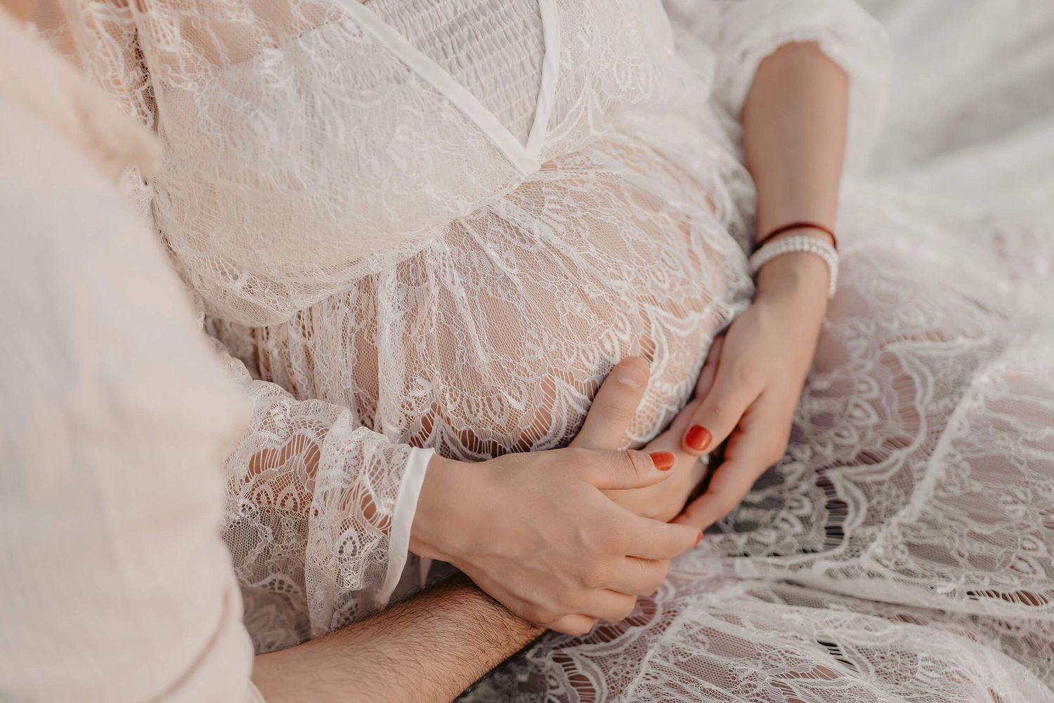 Close-up details of a delicate white lace wedding dress showing intricate patterns and soft tulle fabric and a pregnant belly.