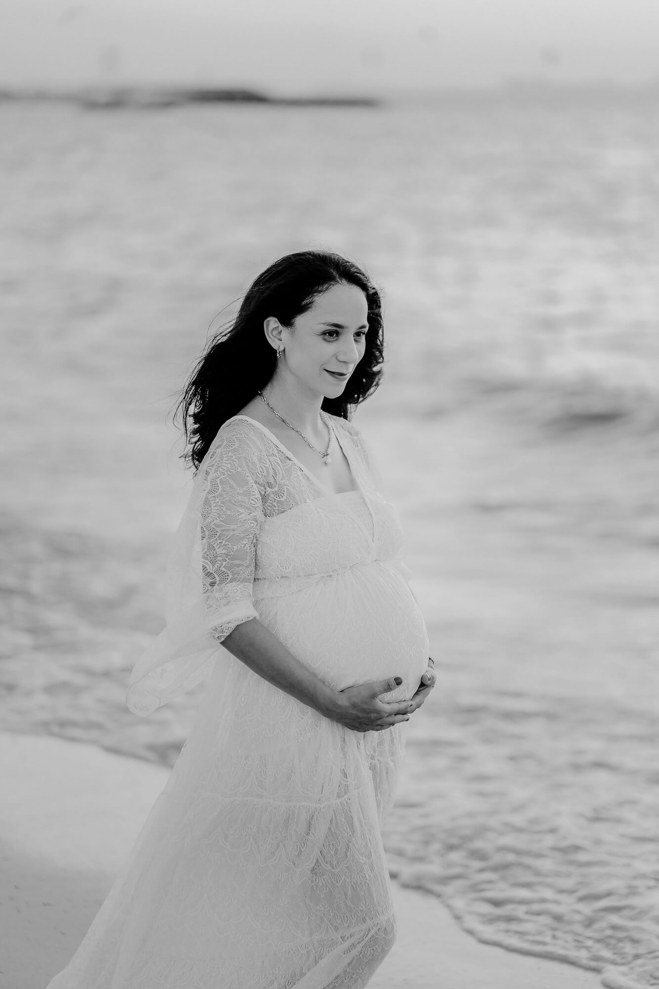 Beautiful black and white maternity photos taken at a misty beach, showing a flowing white lace dress.