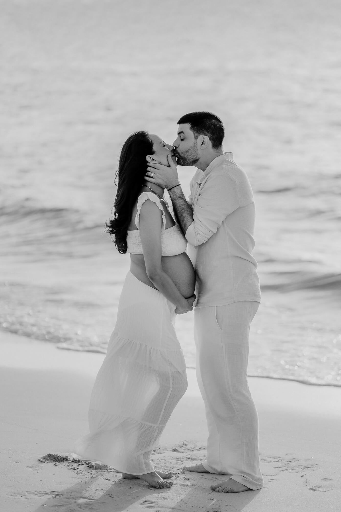 A romantic couple shares intimate moments in a series of black and white photos on a sandy beach.