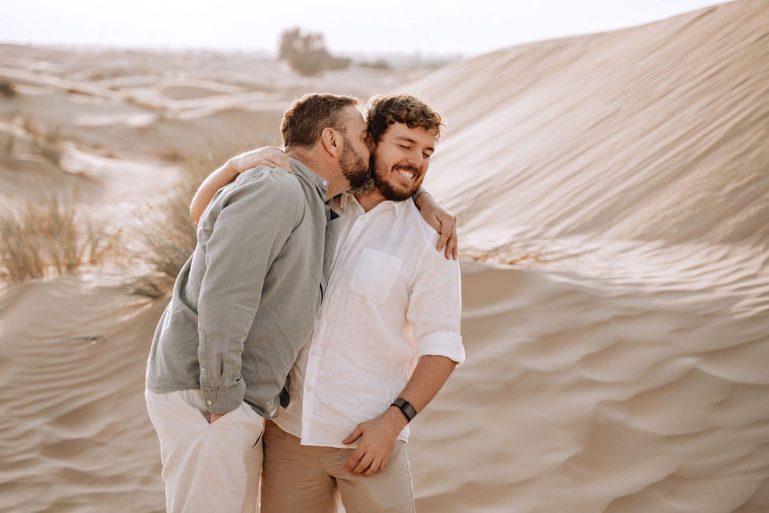 Candid desert photoshoot showing joyful interaction between two people on sand dunes.