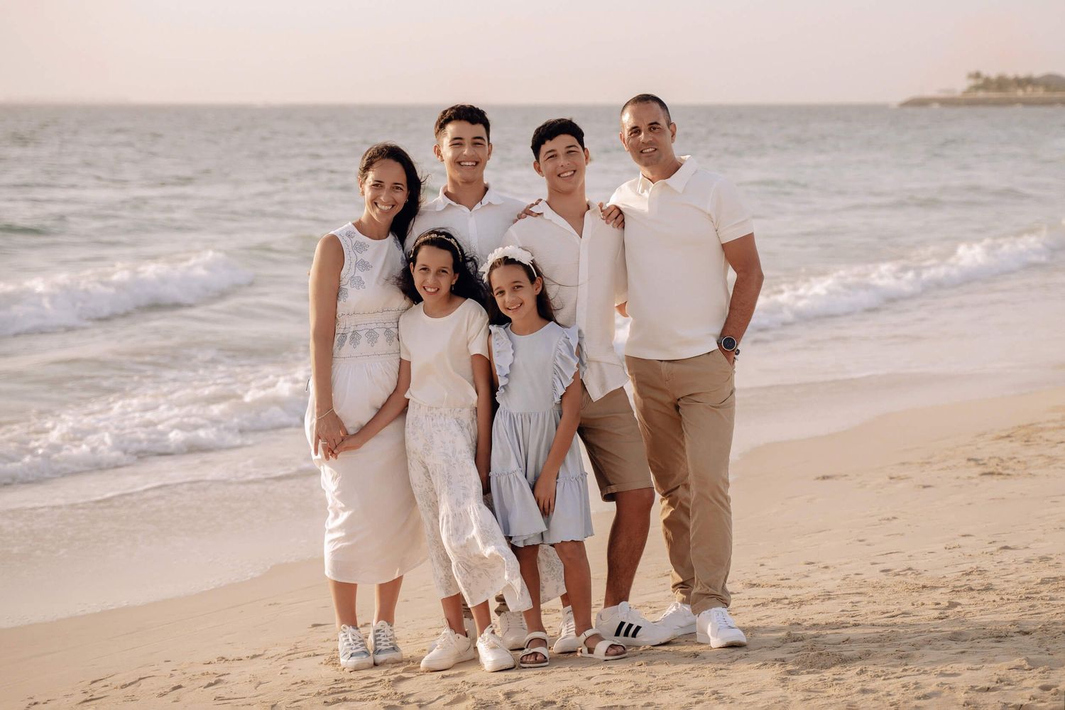 Family standing together on beach in coordinated outfits during golden hour.