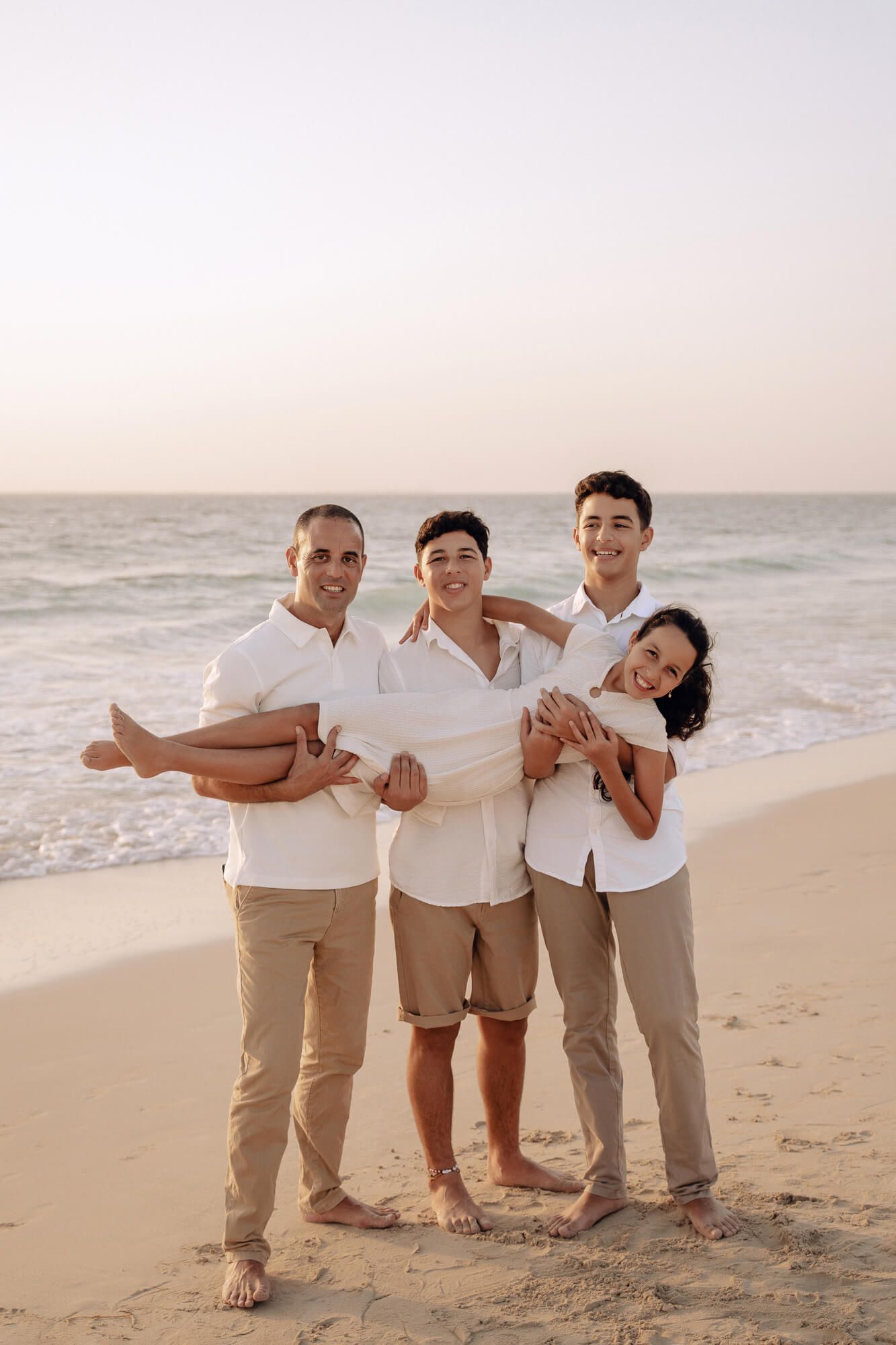 Fun family beach portrait with members in matching outfits lifting and playing together.