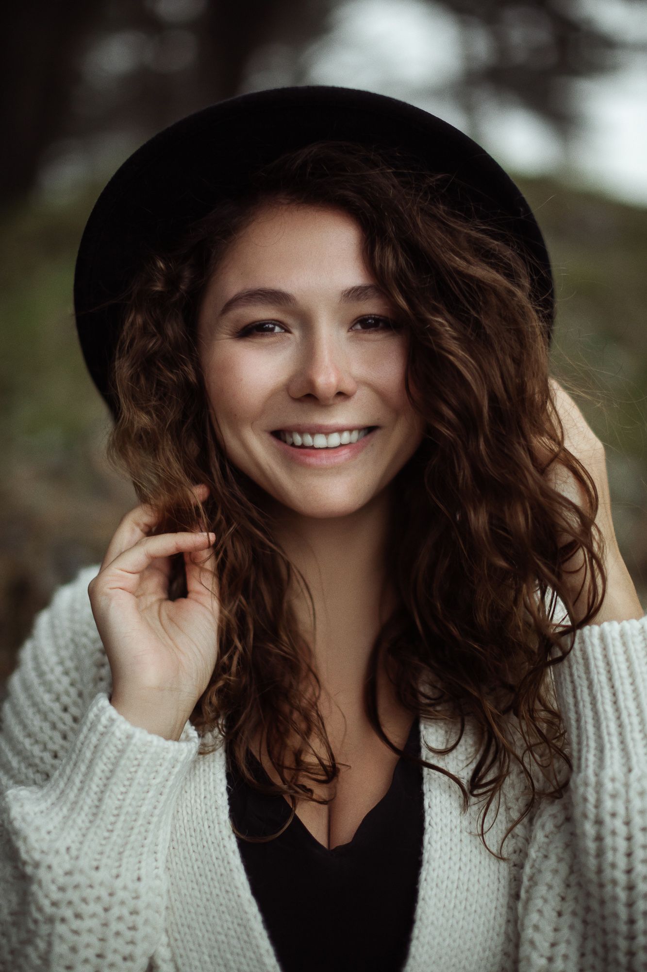 Portrait of person wearing black hat and white sweater with natural curly hair and warm smile.