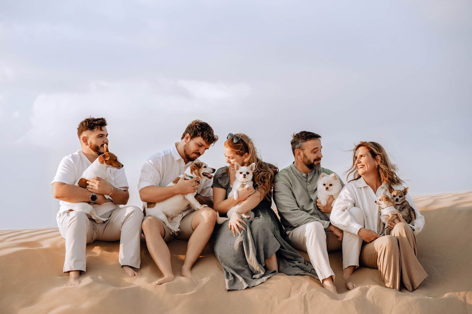 Group arranged on sandy dune holding pets while wearing coordinated neutral colored clothing.