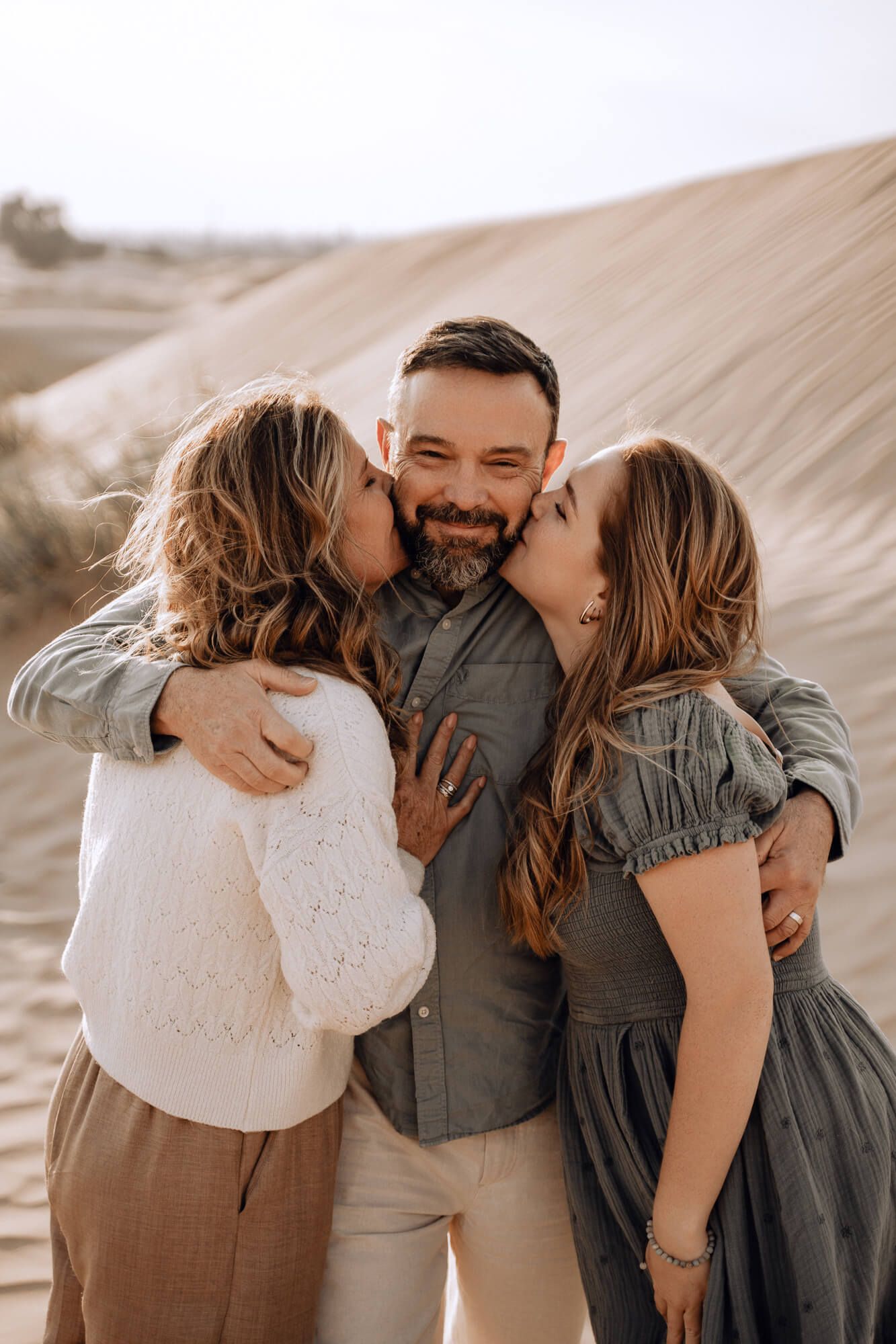 Intimate family moment captured in warm tones as three people share embraces against desert landscape.