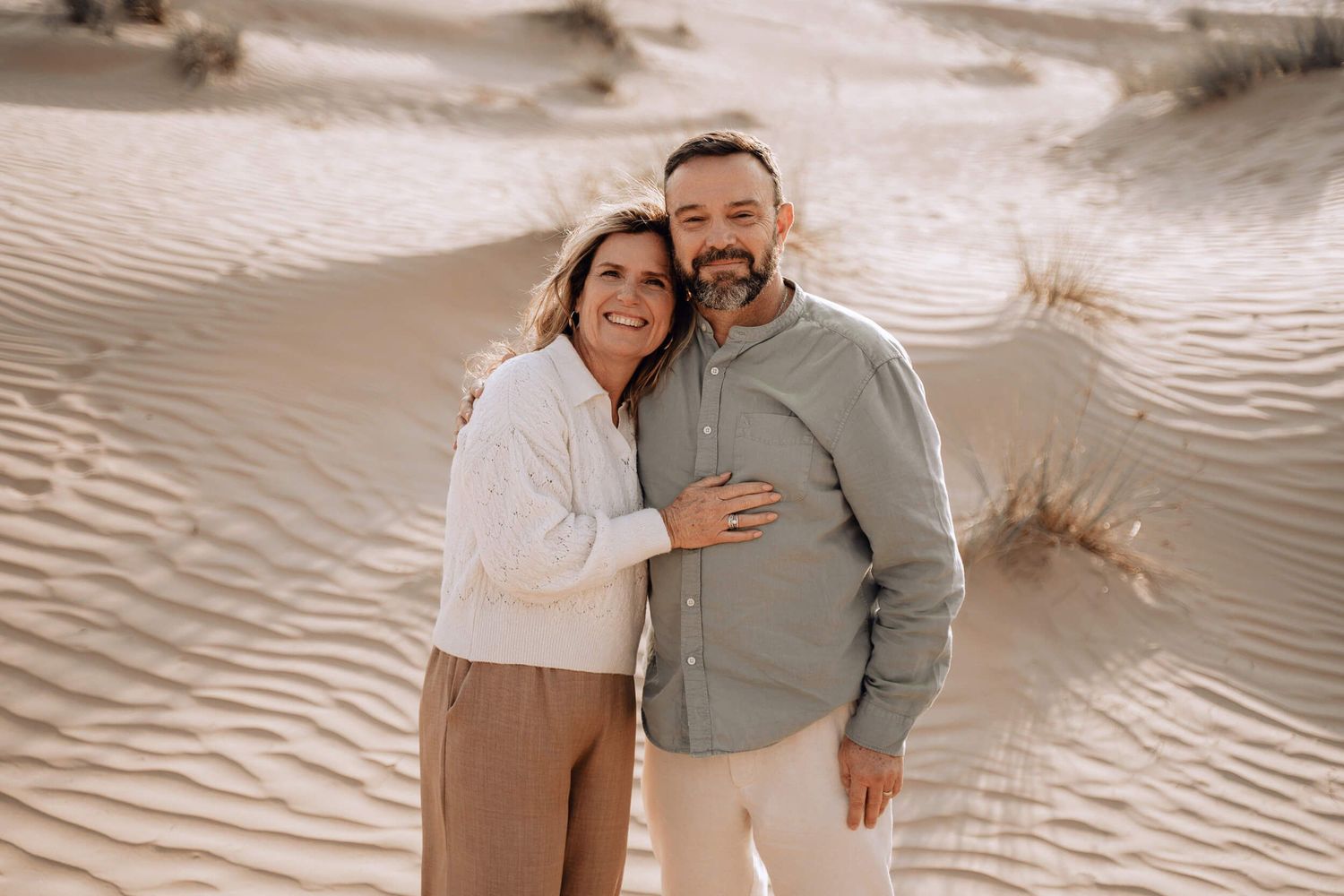 Couple in casual clothing embracing while standing on rippled sand dunes.