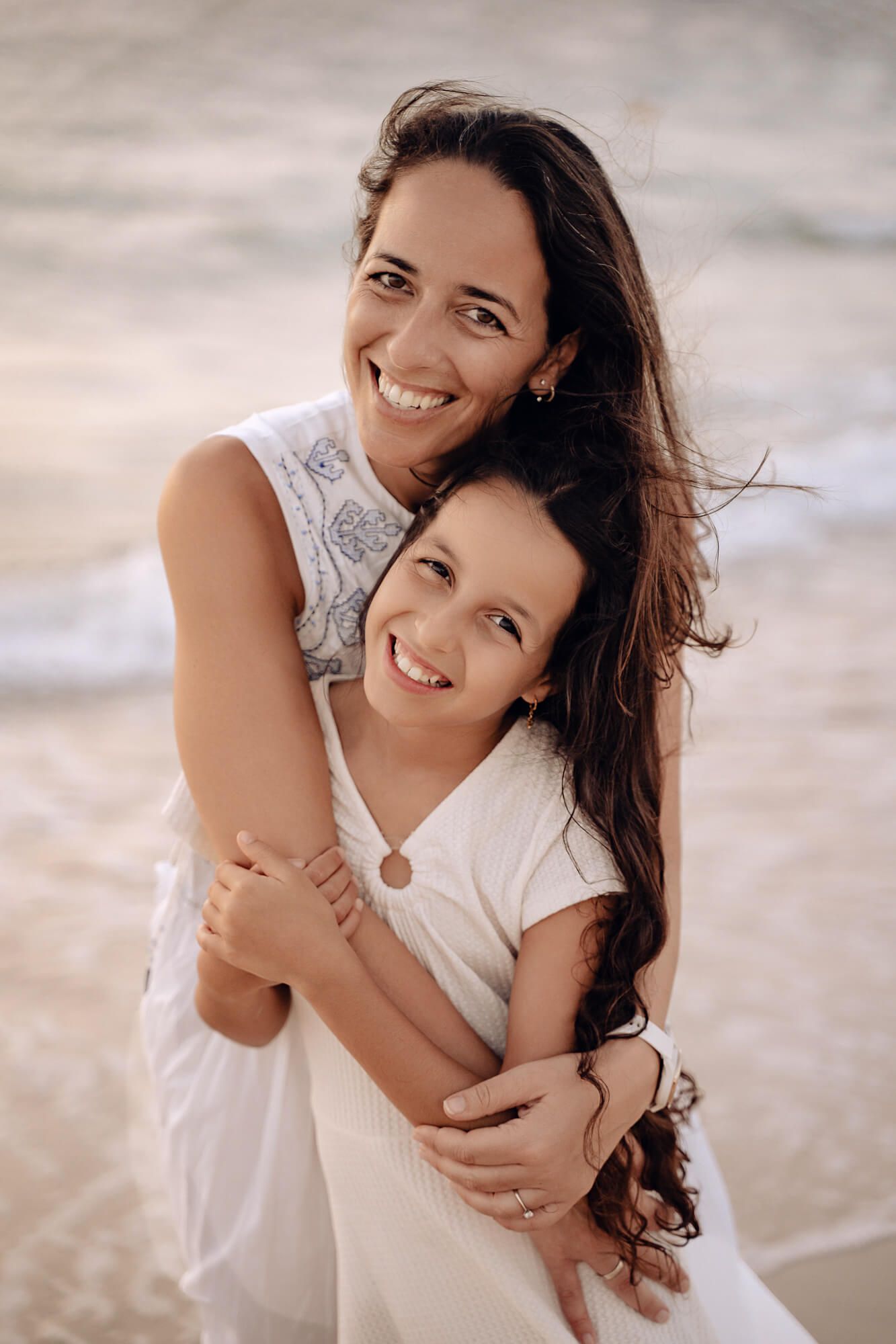 Two people in white outfits share loving embraces on a sunlit beach.