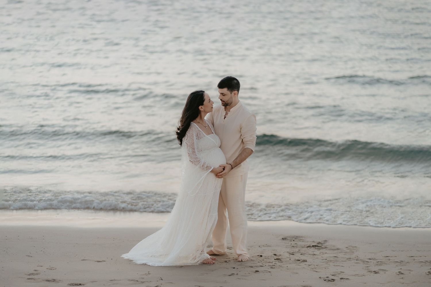 A romantic couple in wedding attire shares intimate moments during a sunset beach photoshoot session.