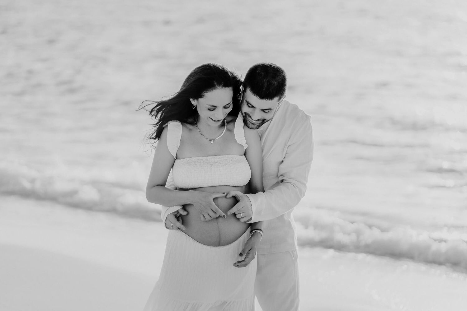 A couple embraces on a sandy beach in a black and white romantic maternity photo session.