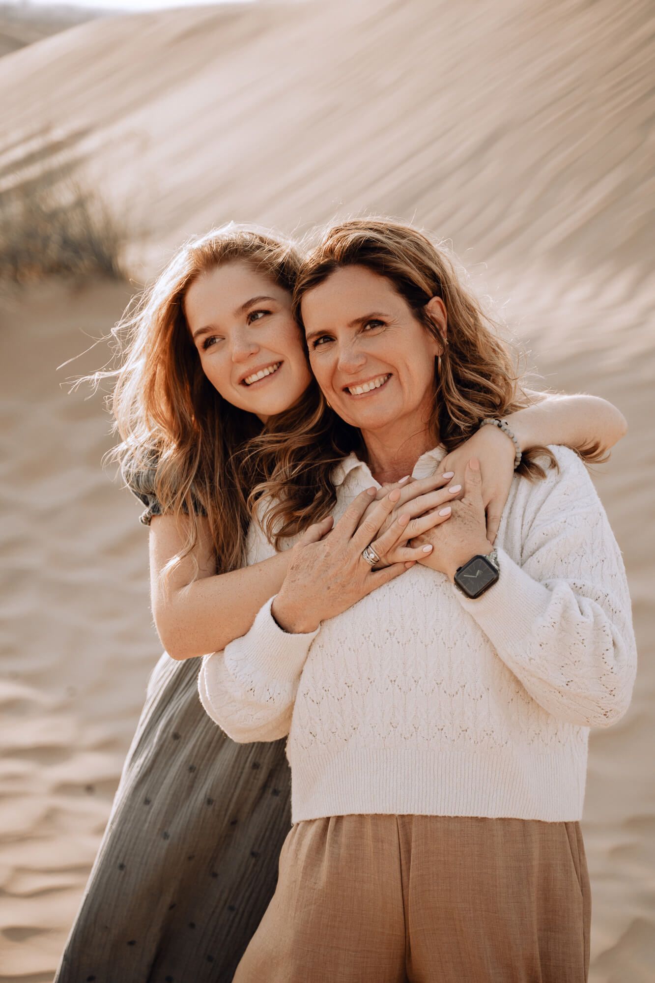 Mother and daughter share emotional embrace while posing against desert landscape.