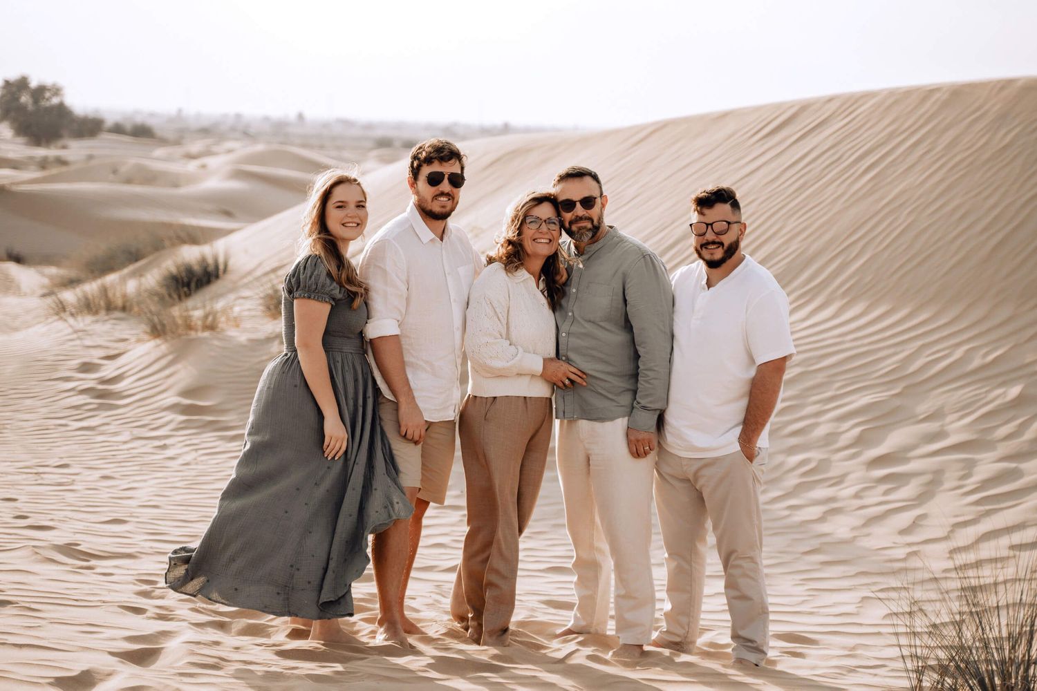Casual group photo of five people posing on sandy dunes in neutral-colored clothing.
