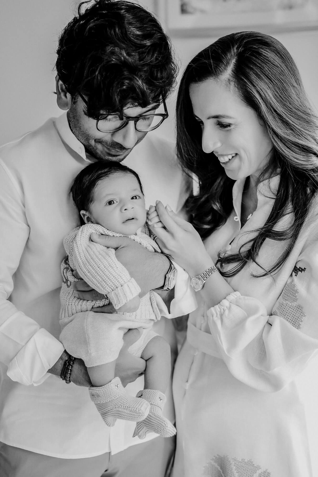 Black and white portrait of parents sharing a sweet moment with their infant baby.