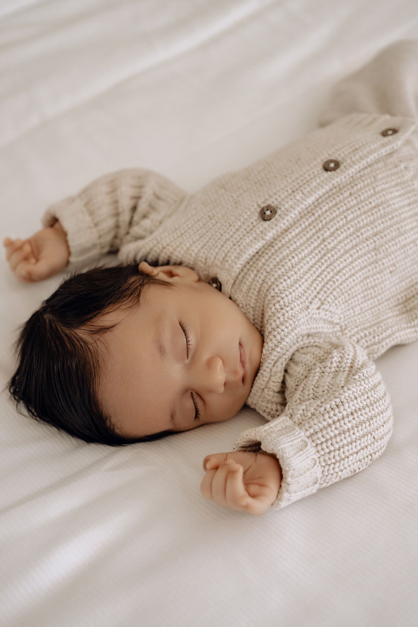 Serene sleeping baby in cream knit sweater on white bedding.