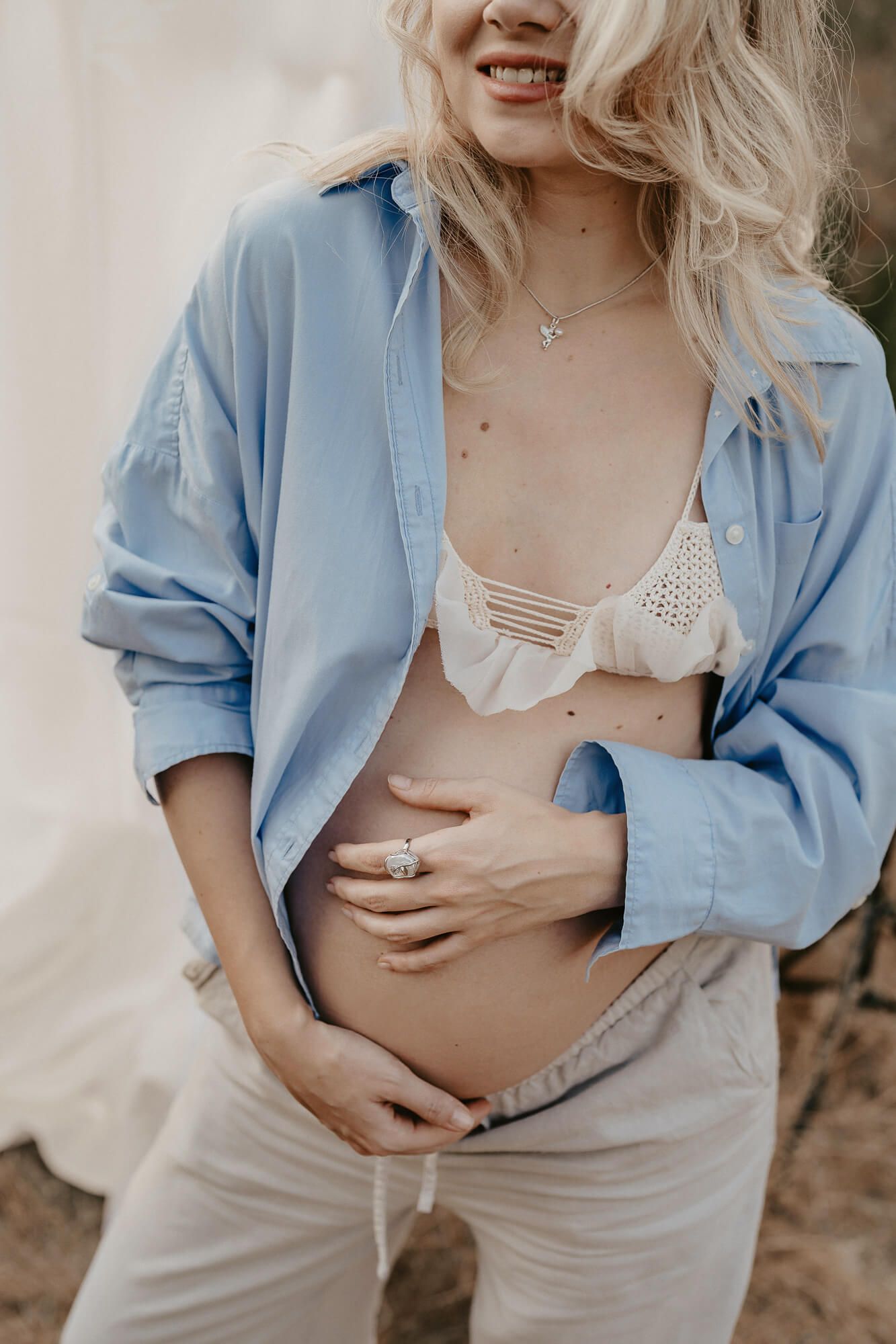 Maternity portraits showcasing pregnant woman in light blue shirt against natural backdrop.