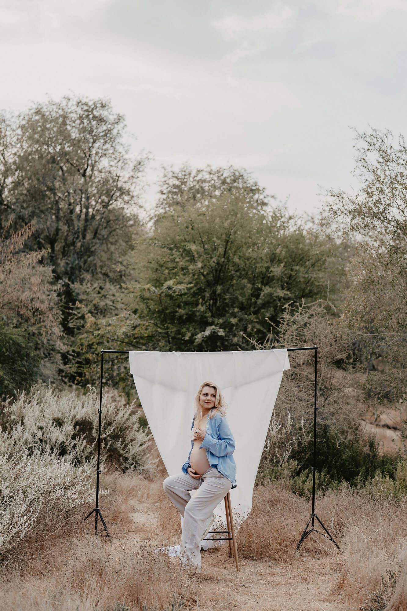 Outdoor maternity photoshoot setup with white backdrop in a natural wooded setting.