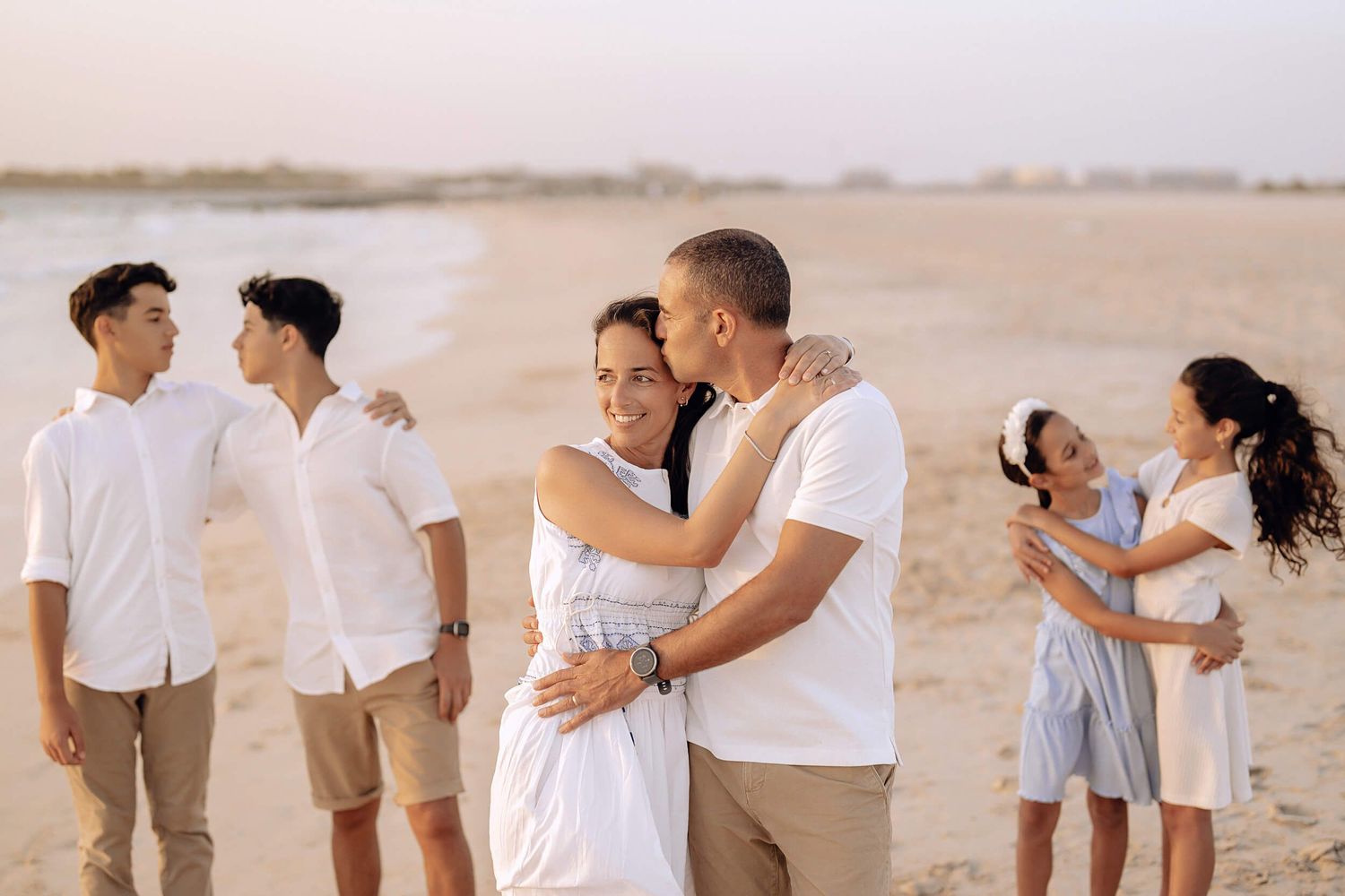 Three pairs of people embracing on beach during golden hour photography session.