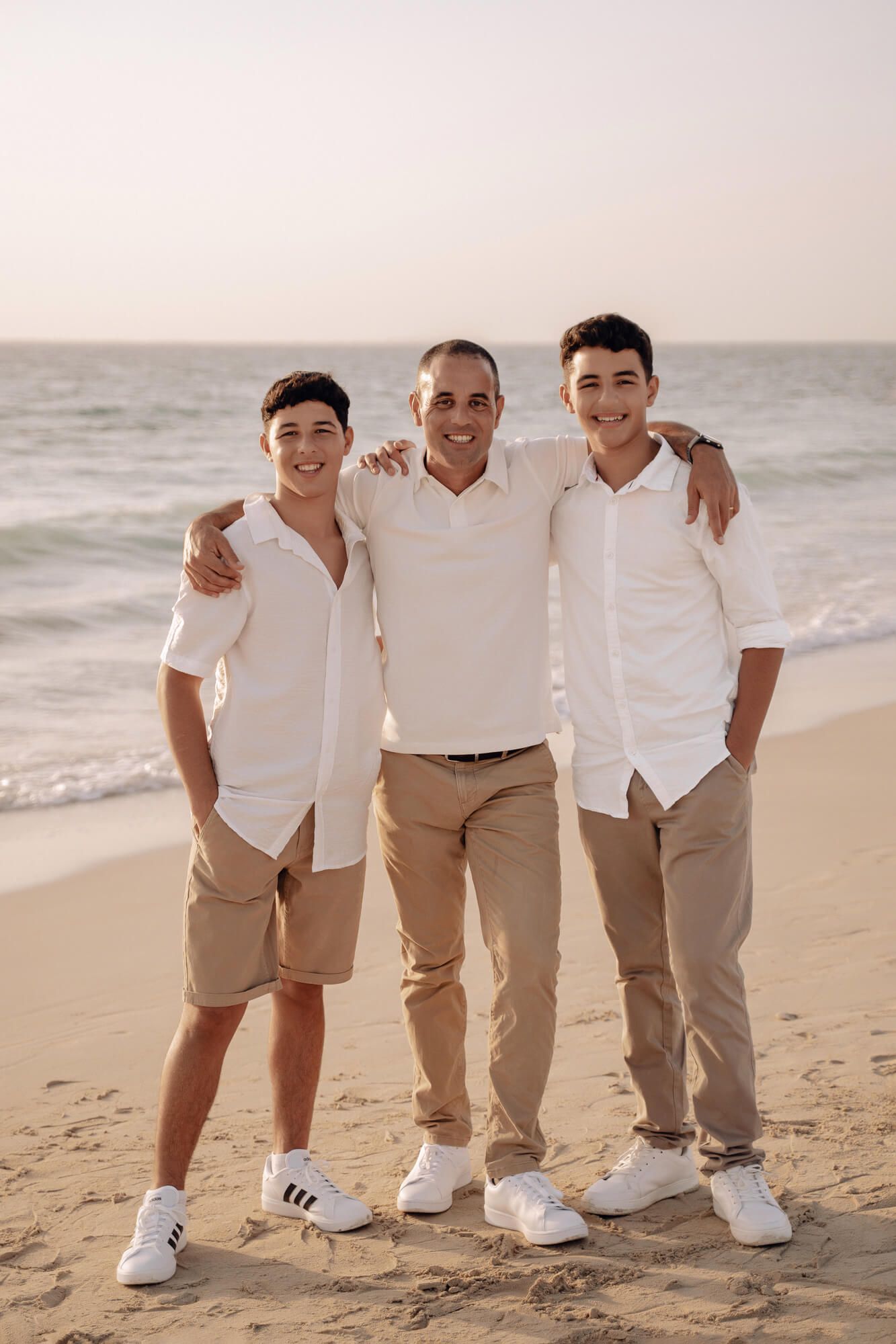 Family group wearing matching white shirts and khakis posing casually on a sandy beach.