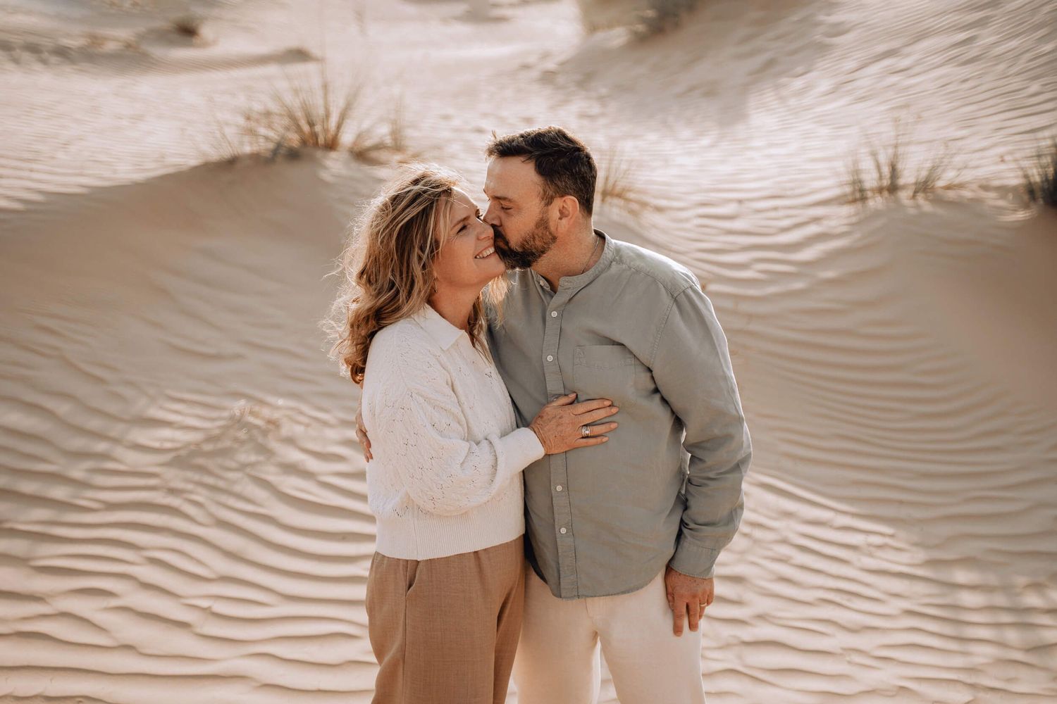 Collection of candid moments between couple embracing on sandy dunes in sepia tones.