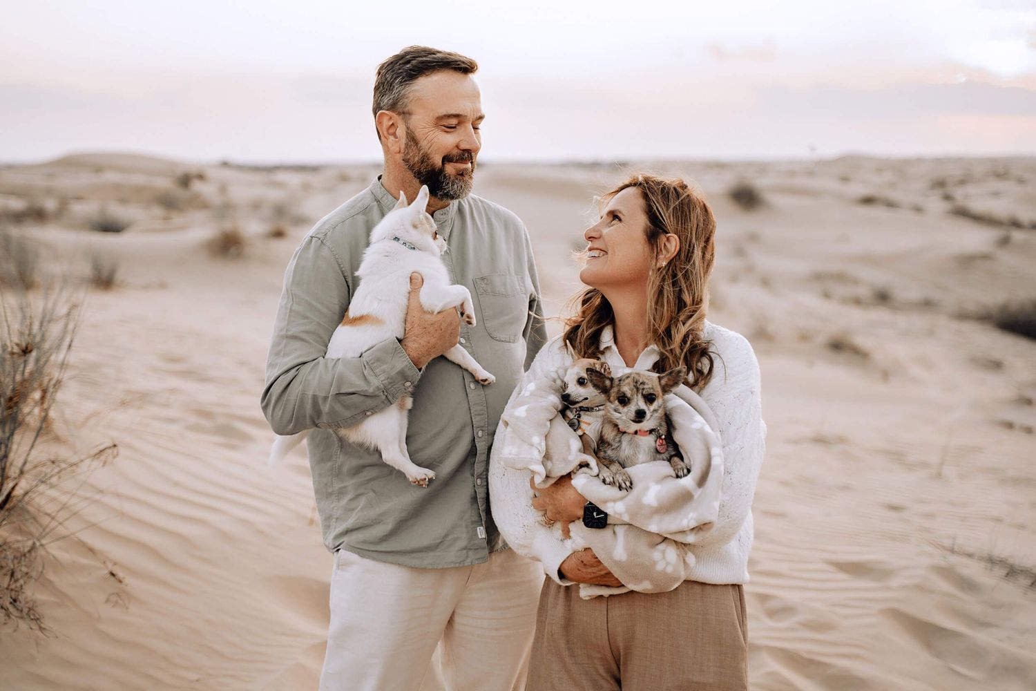 Couple shares tender moment with their chihuahua dog against desert backdrop.