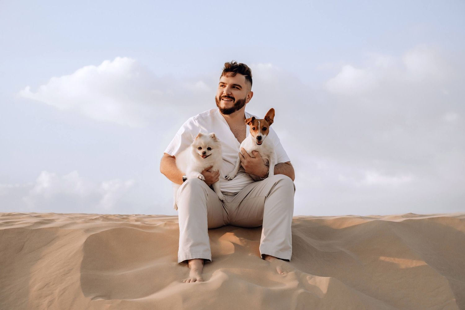 Two small dogs posing on scenic desert sand dunes during daytime.