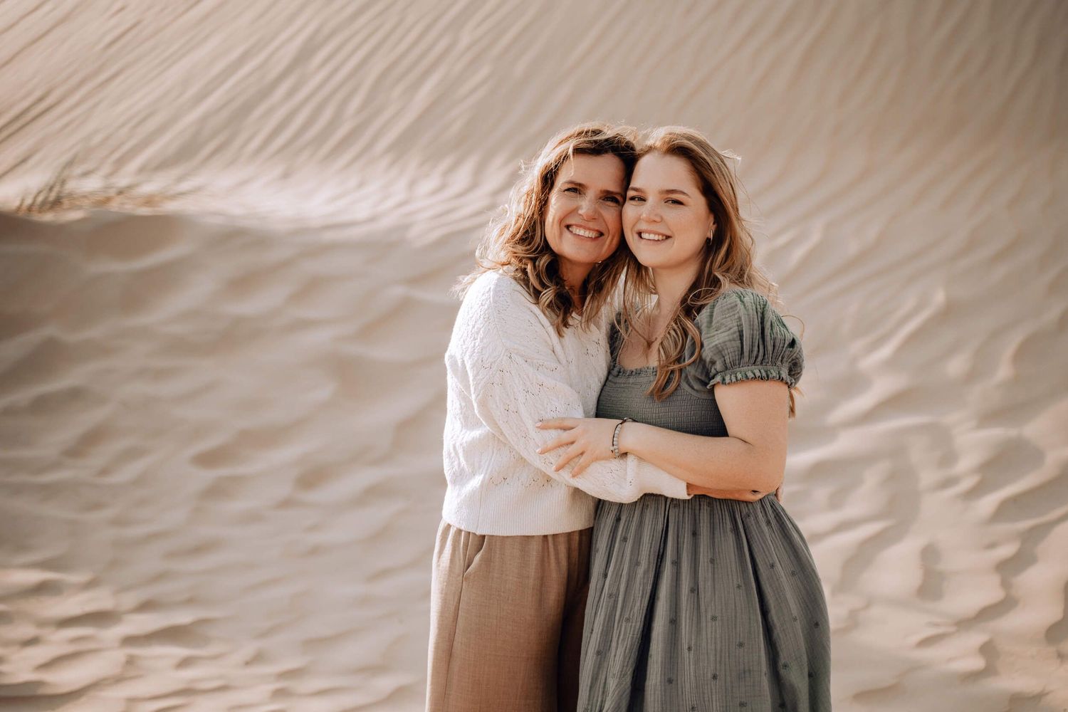 Two people share a warm embrace and genuine laughter against desert sand dunes.