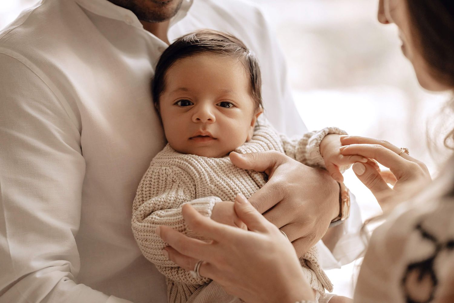 A small infant in a cream knit sweater being cradled in gentle arms.