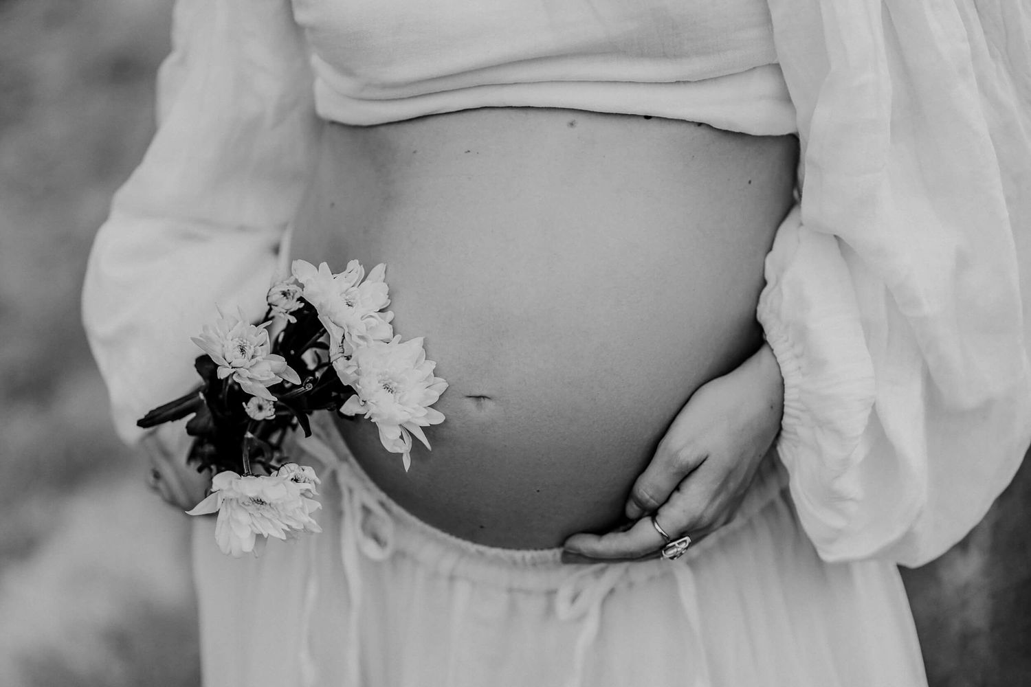 Black and white close-up of a pregnant belly with delicate flowers.