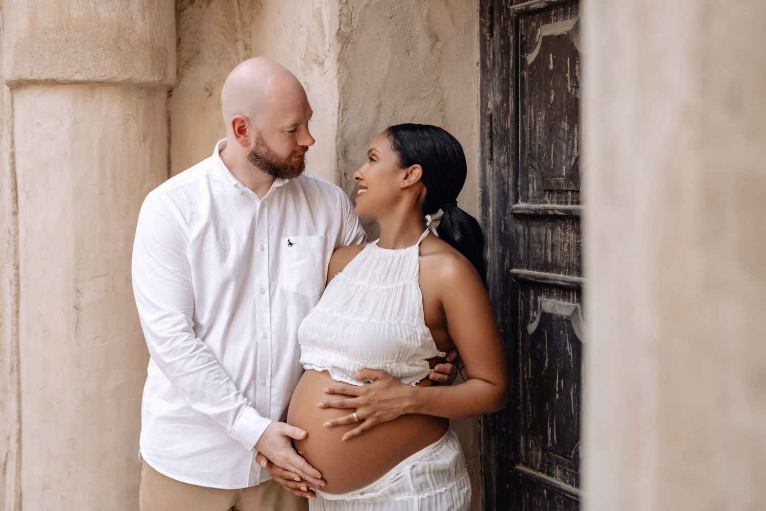 Romantic photoshoot featuring a couple in white clothing against a rustic stone backdrop.