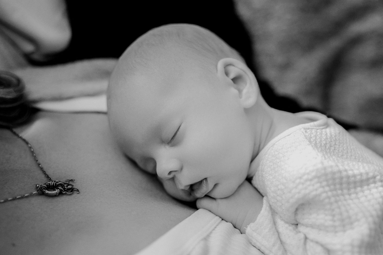 A peaceful sleeping infant in a white outfit rests in black and white photograph.