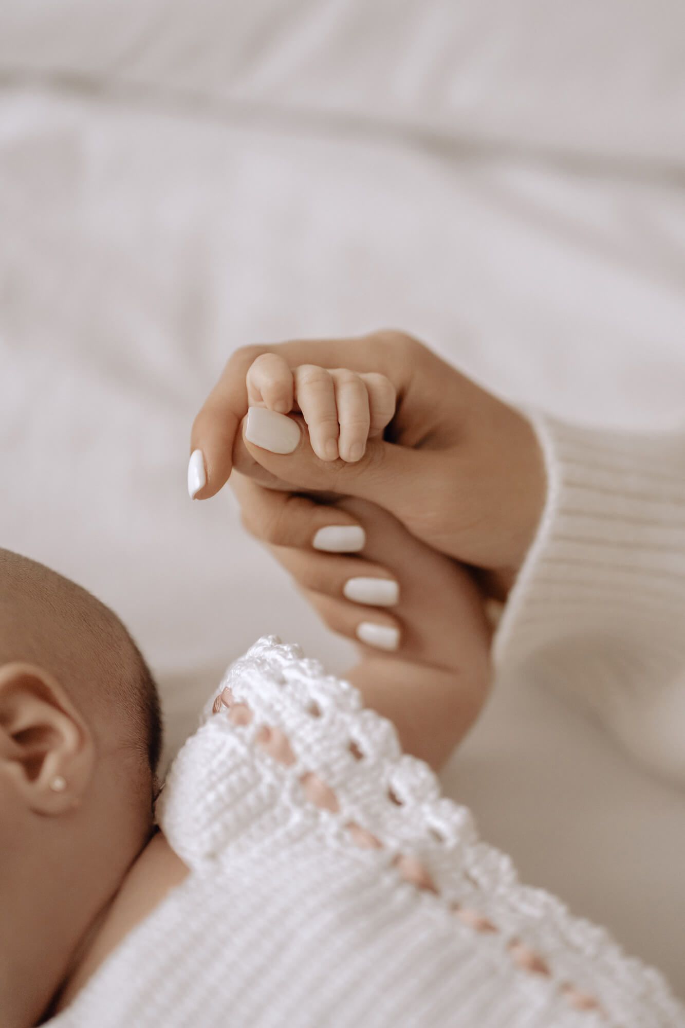 Close up of baby's tiny hand grasping parent's finger with white manicured nails.