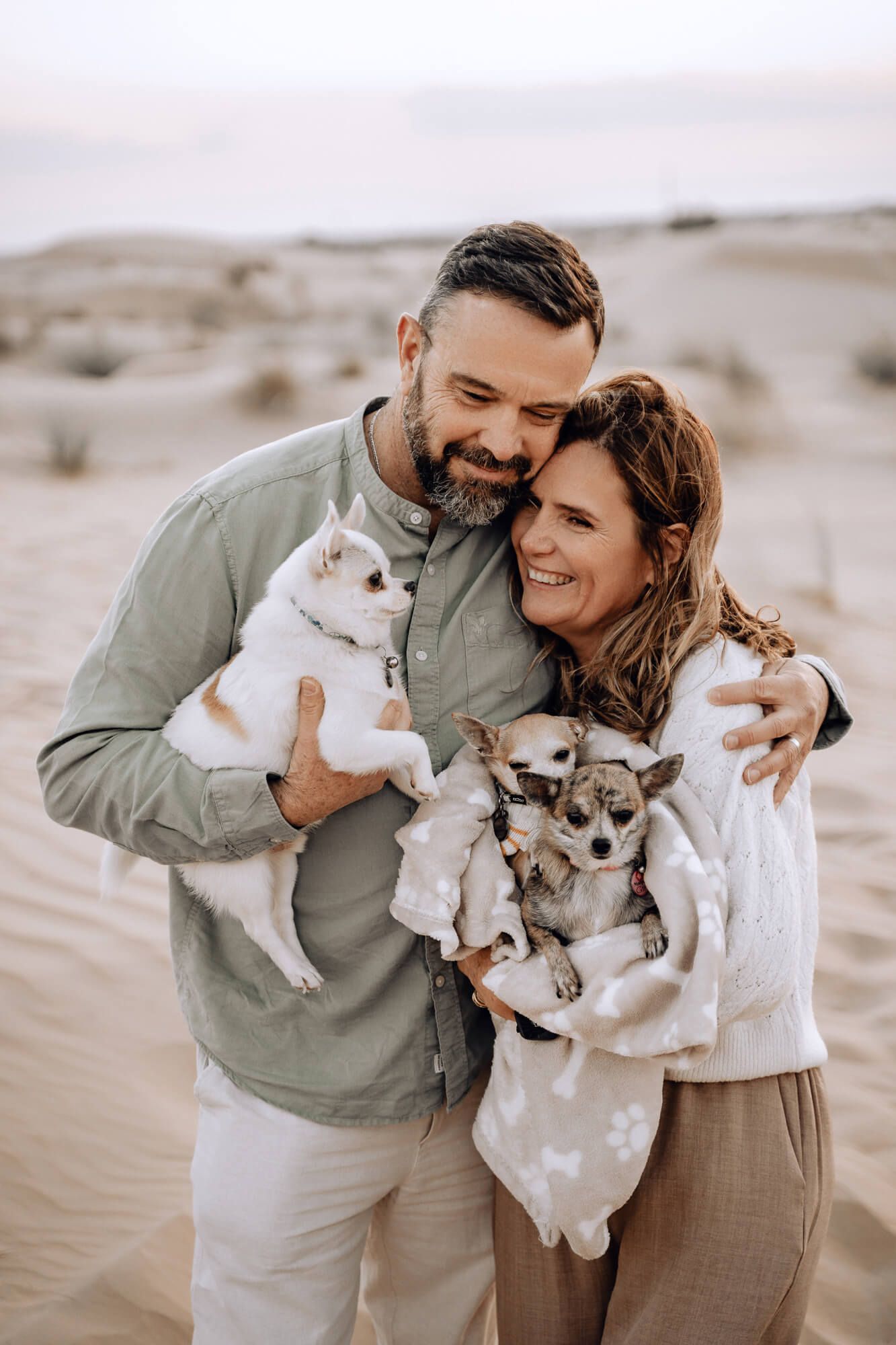 Sweet family portrait with small dog among sandy dunes during sunset.