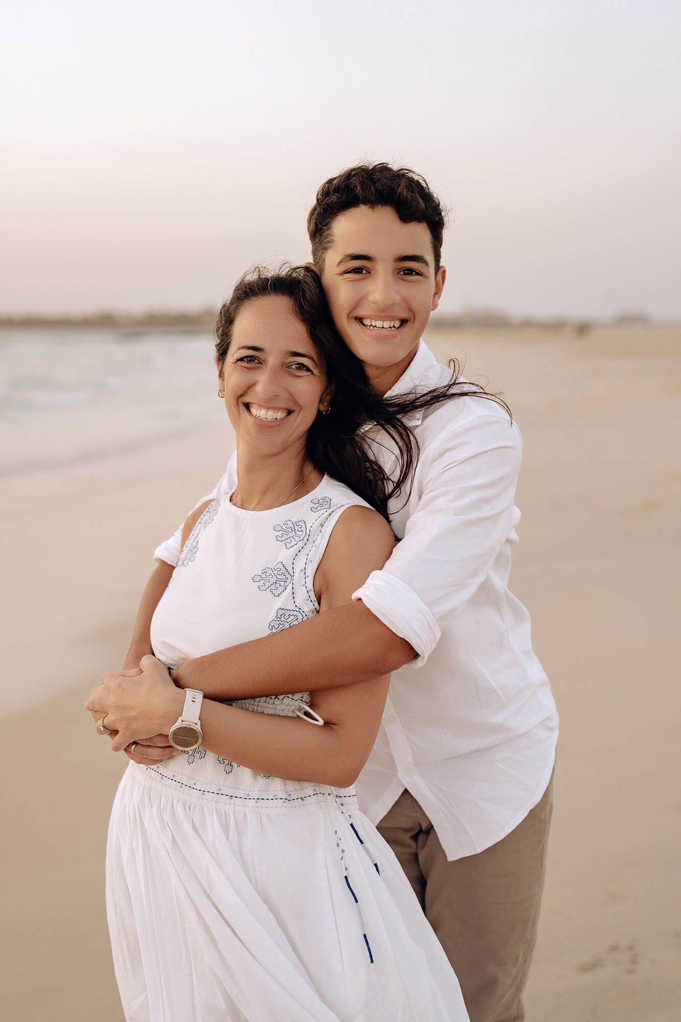 Two people share warm embraces during a casual beach portrait session at dusk.