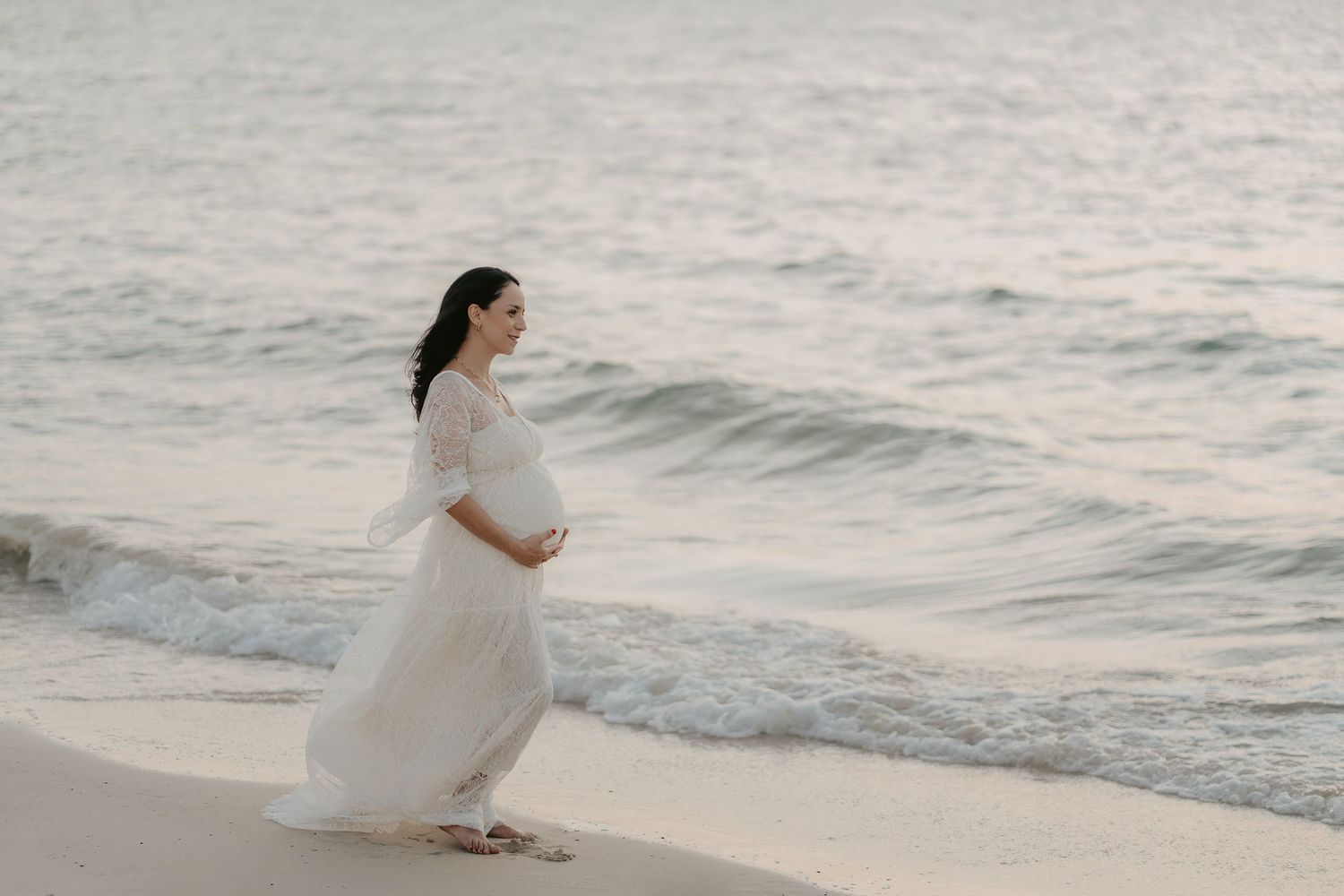 A person in a white wedding dress walks along a serene beach at sunset creating a romantic seaside silhouette.