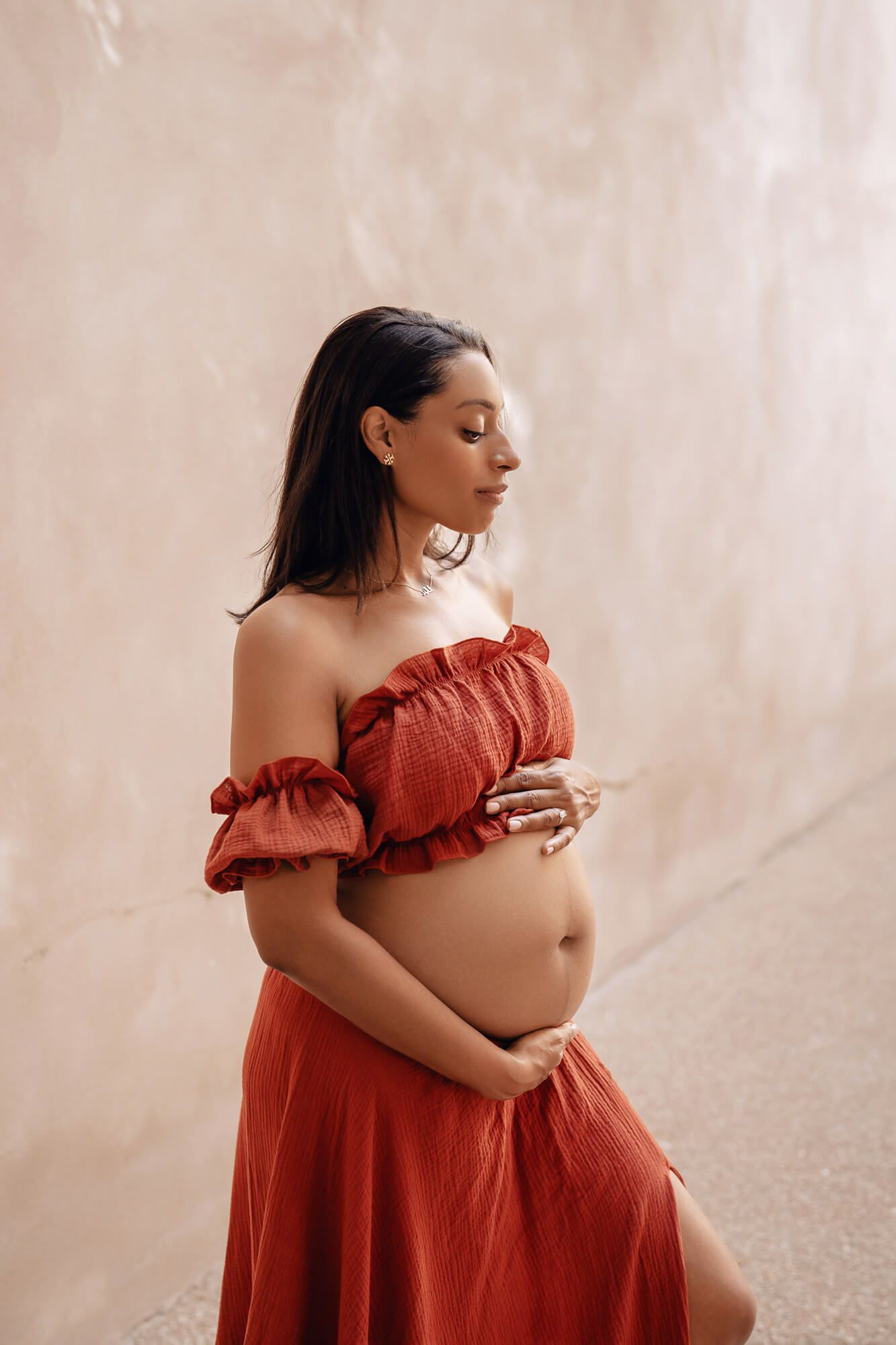 Serene maternity portraits featuring ruched off-shoulder dress against textured wall.