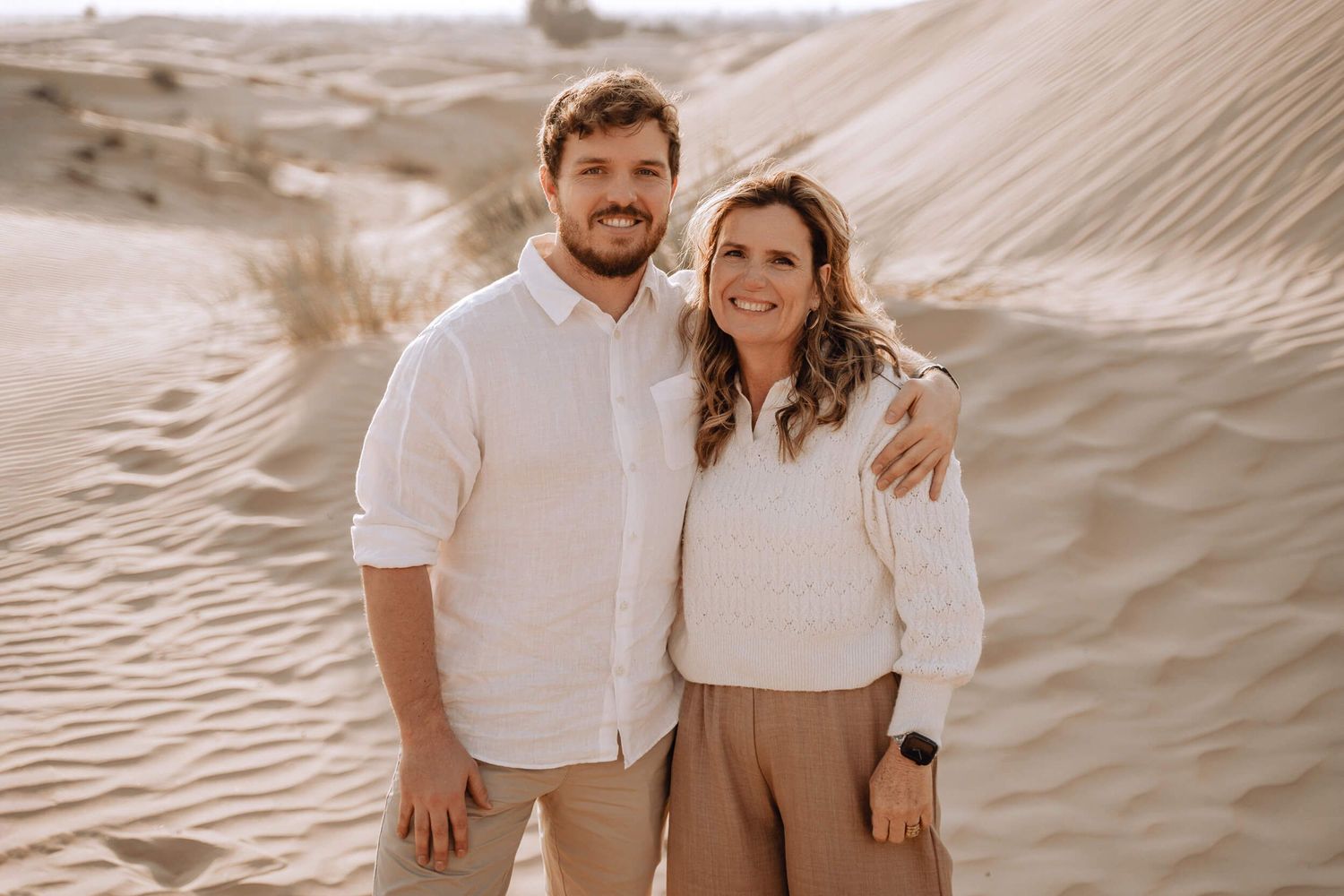 Desert family photography session featuring a couple in light colored clothing against sandy dunes.