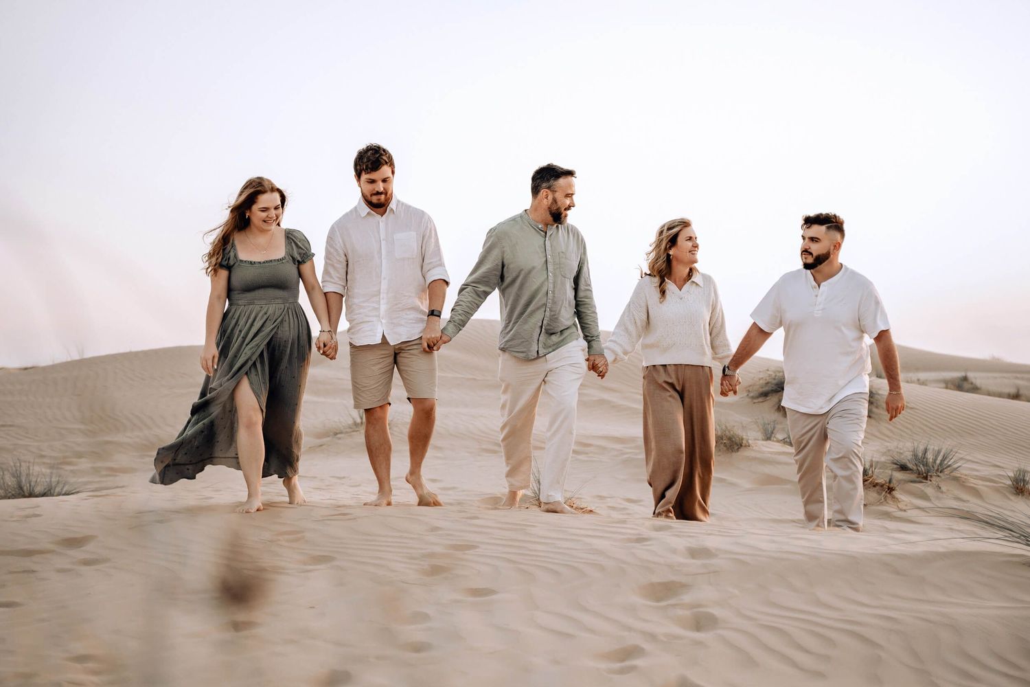 Friends strolling barefoot across desert sand dunes in coordinated neutral outfits.