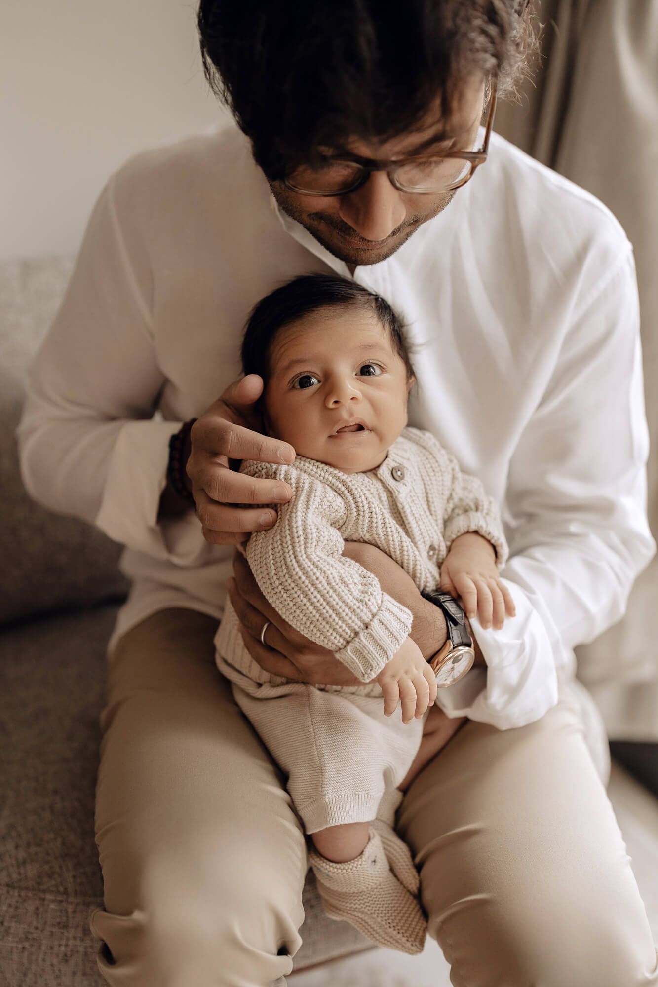 Intimate portrait of parent holding alert baby wearing cream knit sweater.
