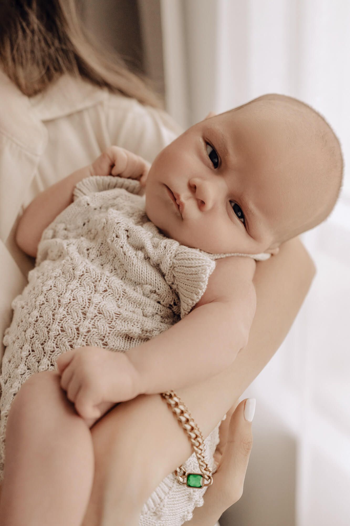 Close-up of a baby wearing a knit cream outfit being held.