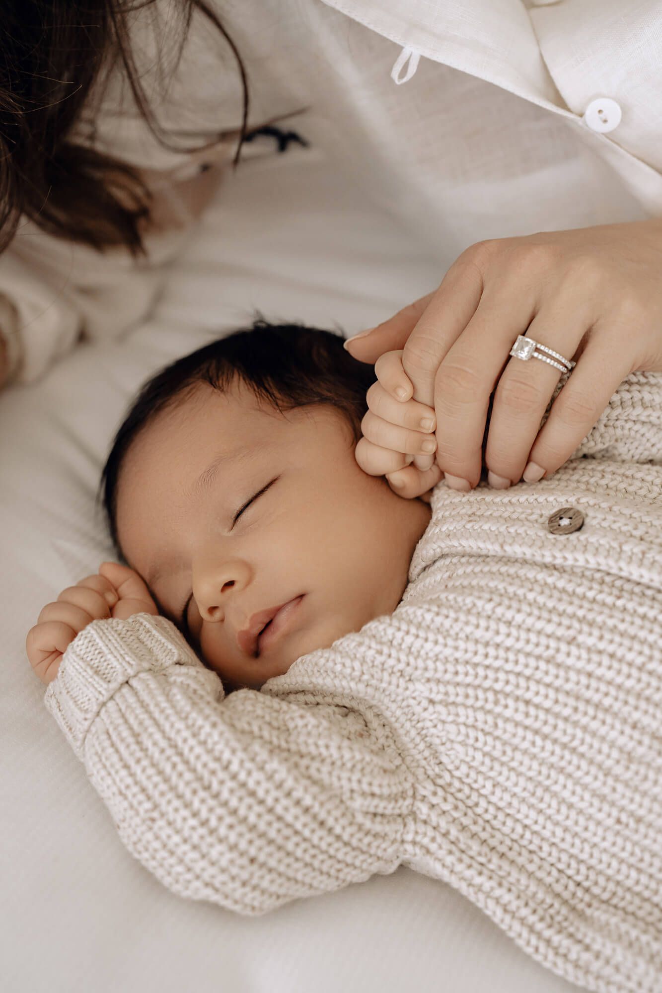 Sleeping baby in white knit sweater lies peacefully on soft bedding.