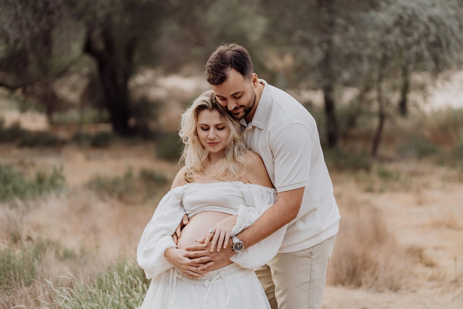 A tender maternity moment photographed in soft natural light on a rustic path.