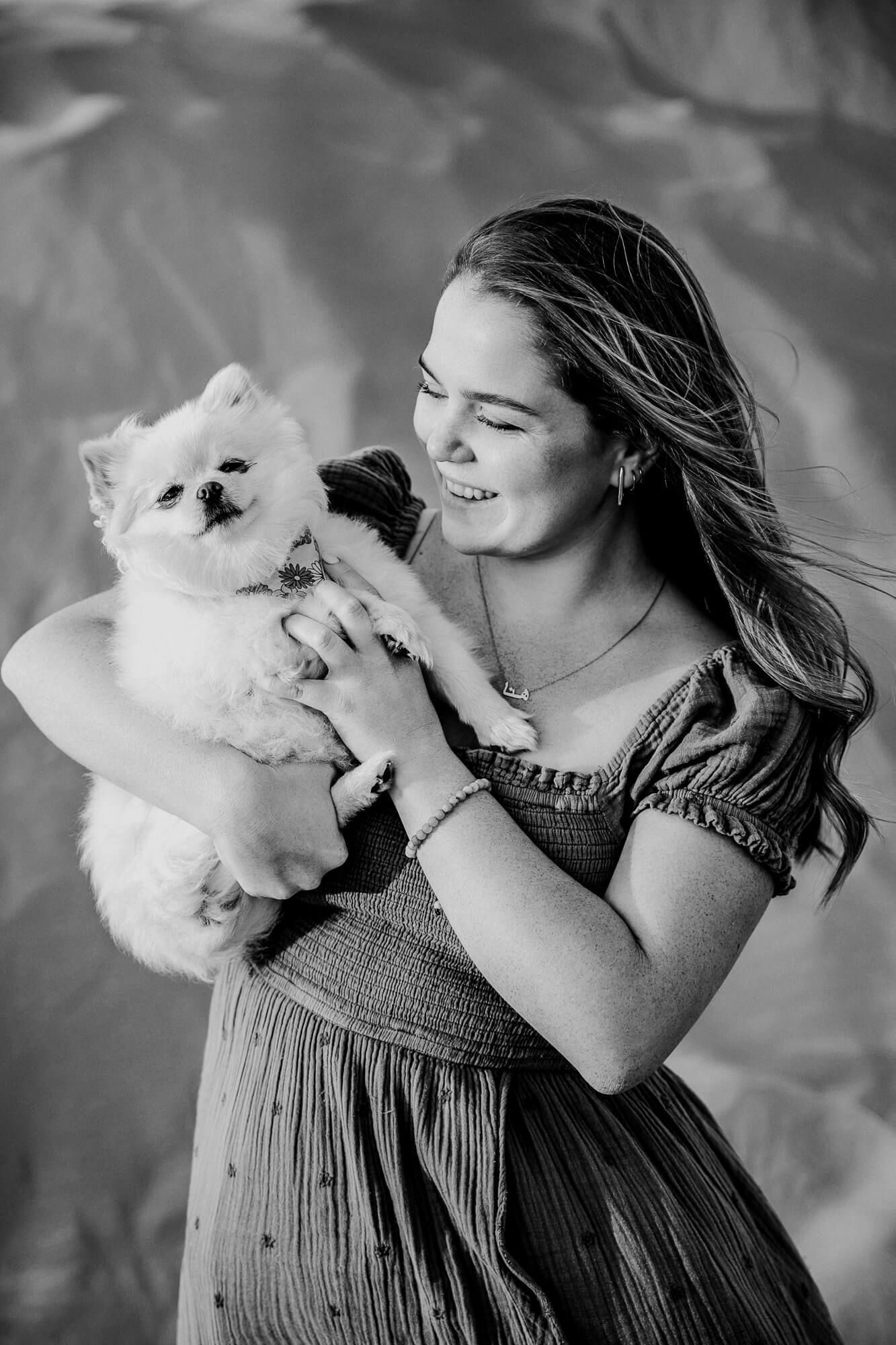 Black and white portrait of person in dress holding and playing with small white dog.