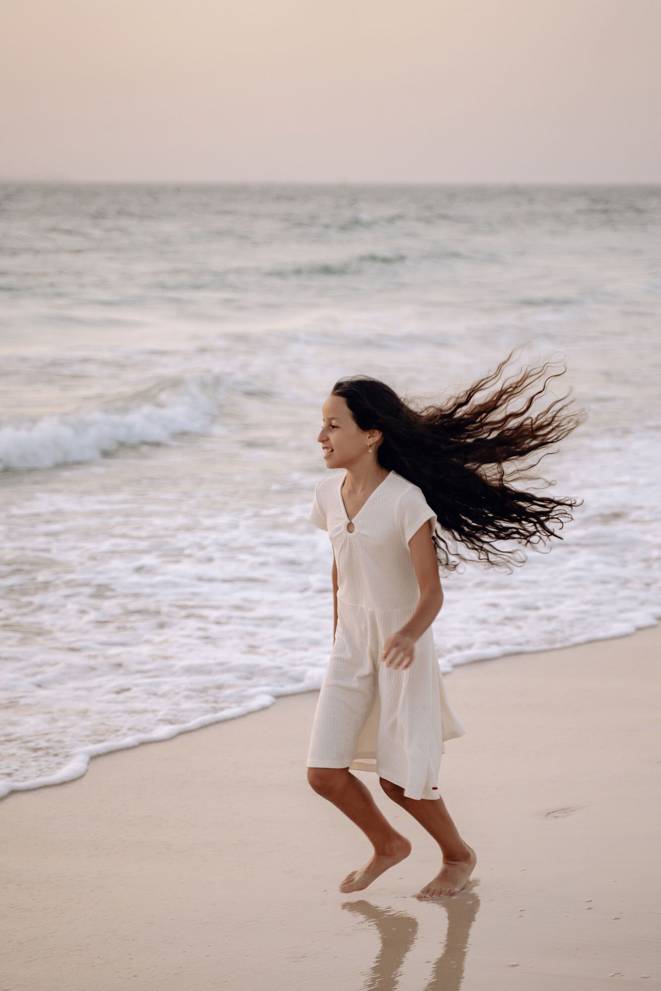 Long dark hair flows in the wind as someone runs joyfully along the beach.