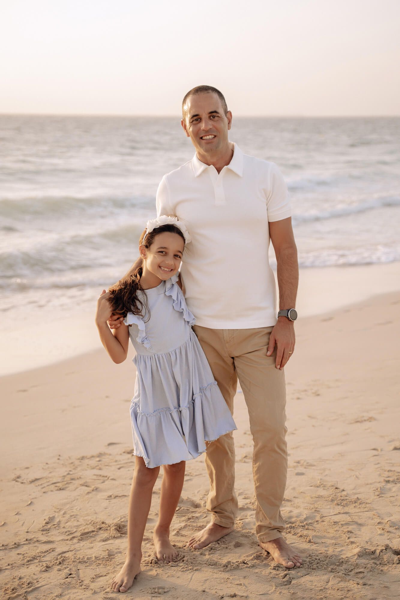 Family shares joyful moments together on sandy beach wearing coordinated casual outfits.