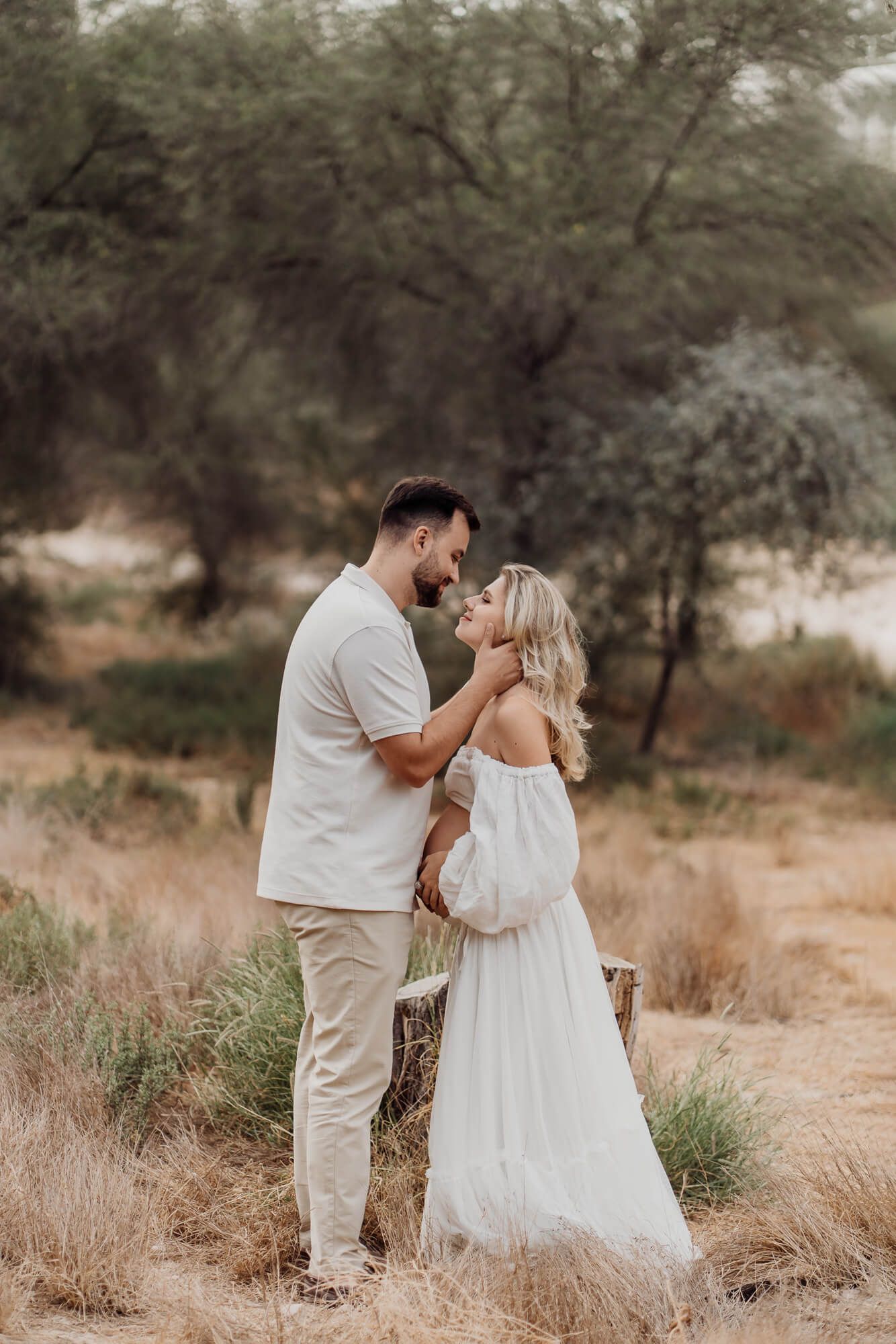 Elegant maternity photoshoot featuring couple in light colored outfits against desert landscape.