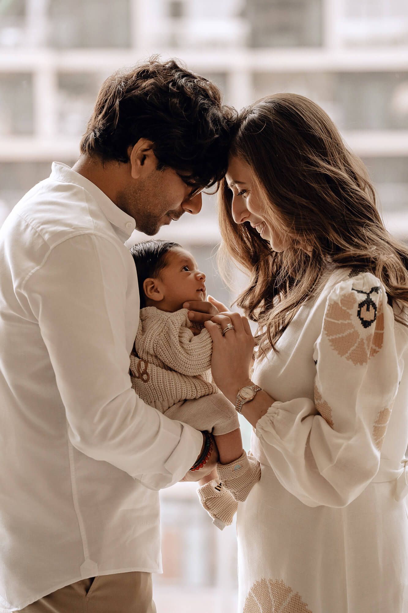 Intimate family portrait with parents in white clothing holding baby between them.