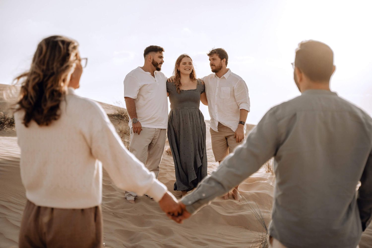 Panoramic series of friends connecting in circle formation on desert sand during golden hour.