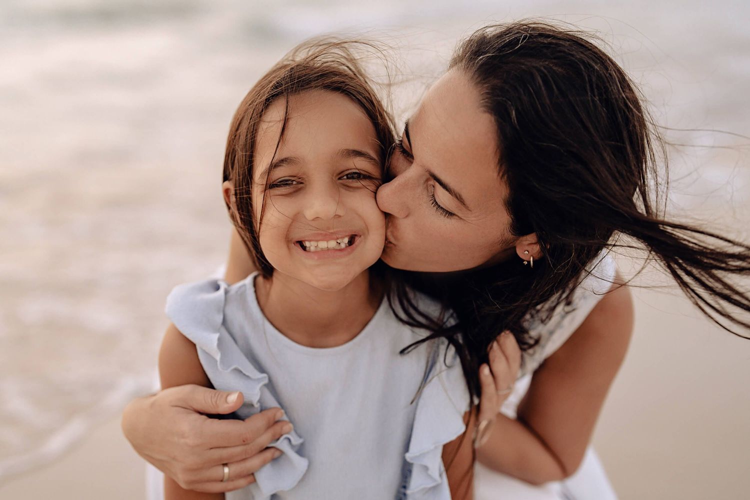Tender family moment captured on a sunny beach with parent and child sharing joy and laughter.