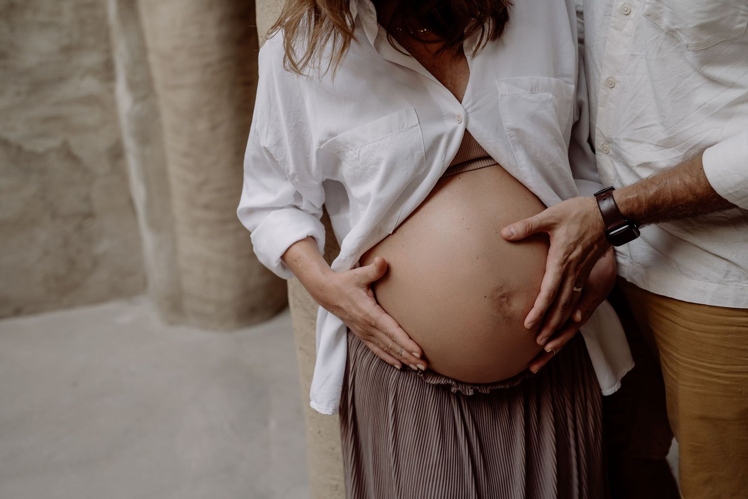 Close-up maternity photography showing hands cradling a pregnant belly.
