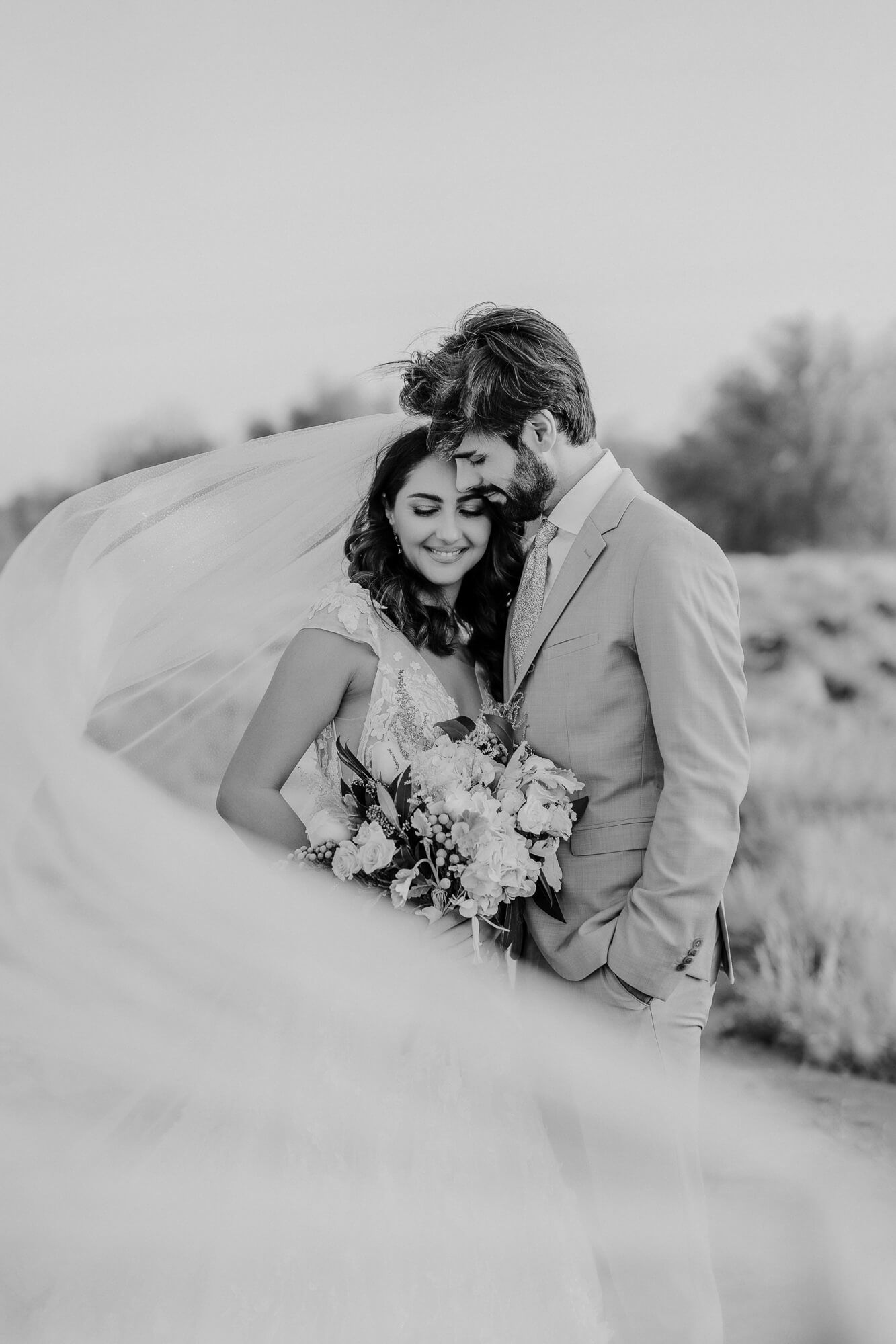 A romantic black and white wedding photo series showing a couple embracing with the bride's veil flowing in the wind.